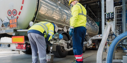Two operators wearing yellow safety protection, helmets and mask at at truck unloading station.