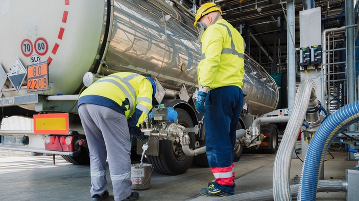 Two operators wearing yellow safety protection, helmets and mask at at truck unloading station.
