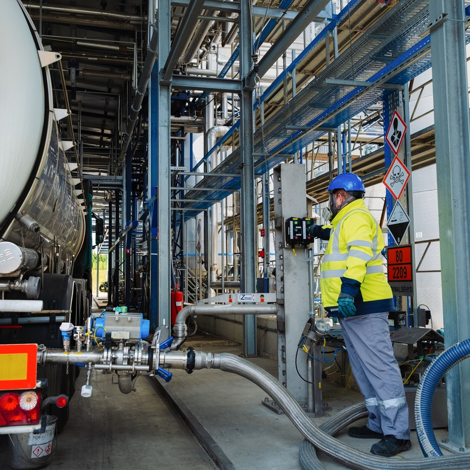 Melamin plant unloading zone with operators in yellow gear and tanks to the right