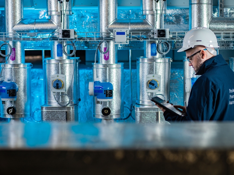 A man looking at a handheld device in front of a wall of Endress+Hauser Devices