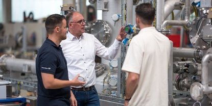 Three people standing in an industrial setting, discussing measurement equipment